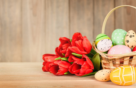a basket with easter eggs and a bouquet of red tulips on a wooden table