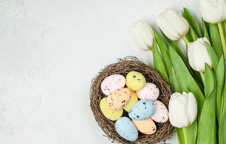 bouquet of white tulips and easter eggs in a nest on a light concrete table, top view, greeting cardの写真素材