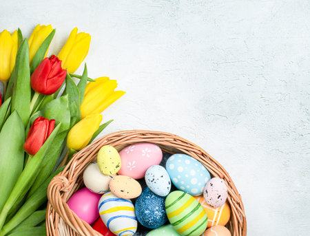 basket with easter eggs and tulips on a light table, top view