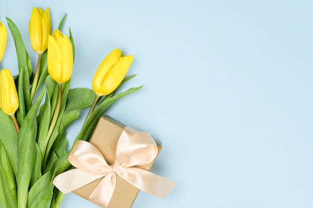a bouquet of yellow tulips and a gift box on a light blue backgroundの写真素材