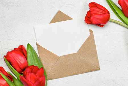 an envelope with an empty note and red tulips on a light concrete table