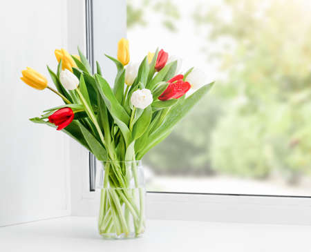 a bunch of tulips in a vase on the windowsillの写真素材