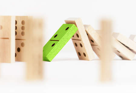 one green wooden domino block resists many other falling dominoesの写真素材