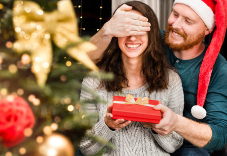 a man makes a surprise to a woman by closing his eyes and gives her a Christmas presentの写真素材