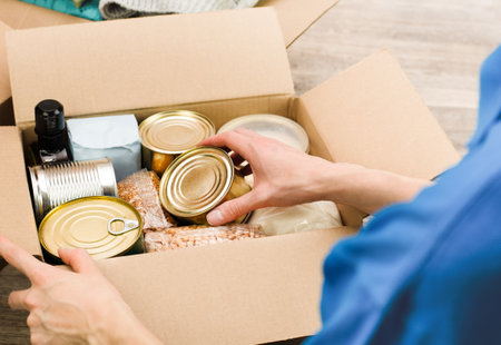 a woman puts groceries in a cardboard box with humanitarian aid, close-upの写真素材