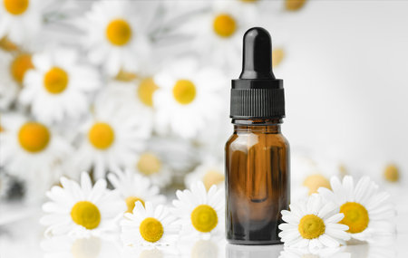 bottle with oil and chamomile flowers around, use of chamomile in spa, cosmetology, aromatherapy and medicineの写真素材