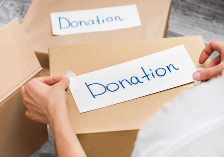 a woman sticks a sticker with the inscription Donations on a cardboard box. help and support for those in needの写真素材