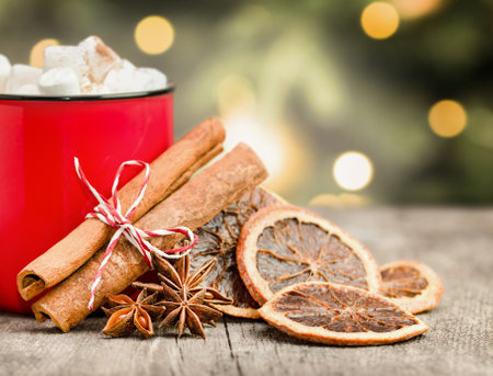 mug with a hot drink, marshmallows and spices on the background of the Christmas treeの写真素材