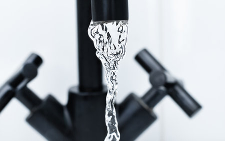 clear water pouring from a black faucetの写真素材