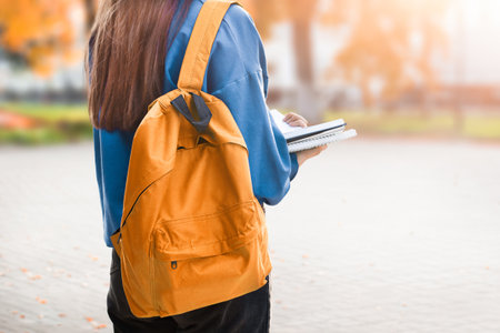 girl student stands on the street with a backpack and reads notes in a notebookの写真素材