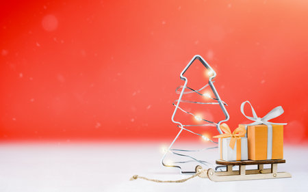 Christmas tree and wooden sleigh with gift boxes on red backgroundの写真素材