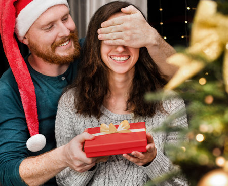 man closes woman's eyes and gives her a Christmas giftの写真素材