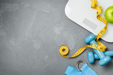 measuring tape, scales, dumbbells, sports belt and apple on gray concrete background, top view