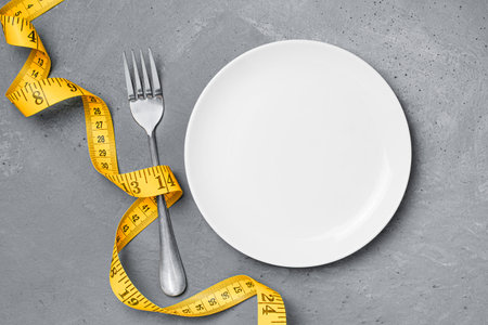 measuring tape, empty plate and fork on a gray concrete background. weight loss and diet conceptの写真素材