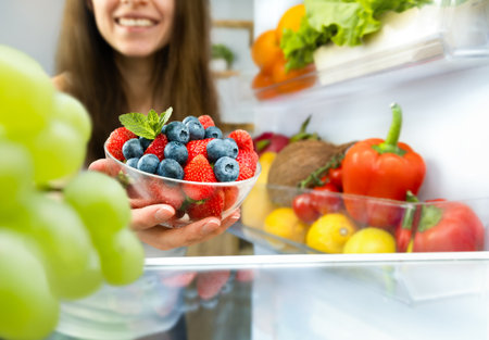 happy woman taking out a plate of berries from the refrigeratorの写真素材