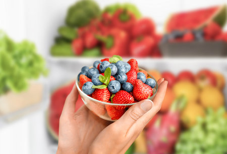 female hands holding a glass plate with berries on the background of the refrigeratorの写真素材
