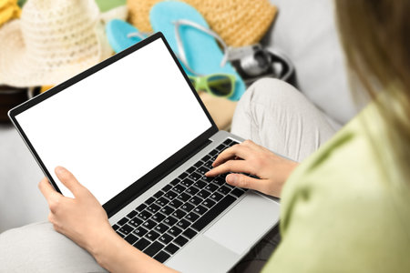 woman with a laptop in her hands sitting on the sofa next to a suitcase of summer clothesの写真素材