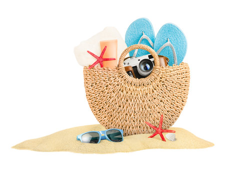 wicker bag with beach accessories in a pile of sand on a white isolated backgroundの写真素材