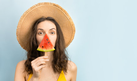 woman with a slice of watermelon on an ice cream stick on a blue backgroundの写真素材