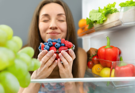 a woman enjoys the smell of fresh berries that she took out of the refrigeratorの写真素材