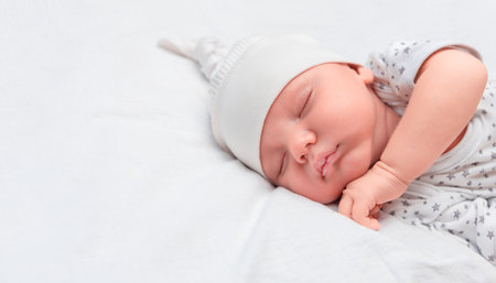newborn baby in pajamas and hat cutely sleeping in bedの写真素材
