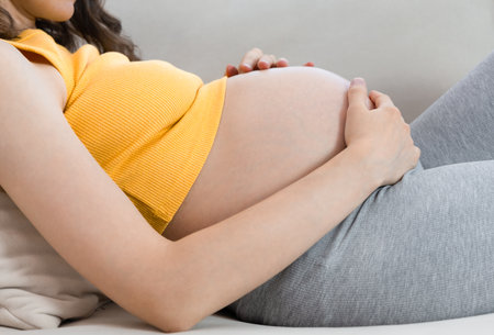 pregnant woman lying on sofa holding her belly, close-upの写真素材