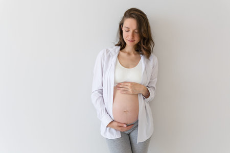 pregnant woman stands in a shirt and holds her belly with her hands