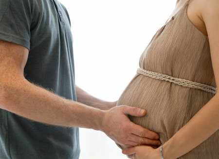 man touching pregnant woman's belly on light backgroundの写真素材