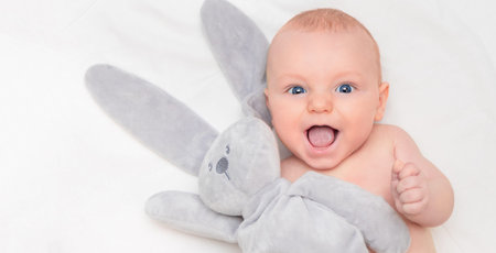 happy baby looking at camera with mouth open and holding toy bunny