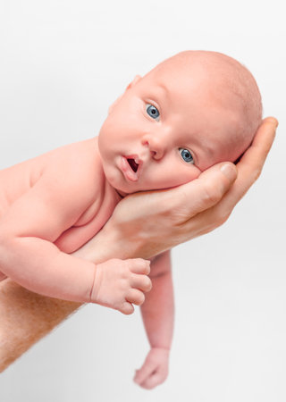cute baby lying on father's palm and looking at camera on light backgroundの写真素材