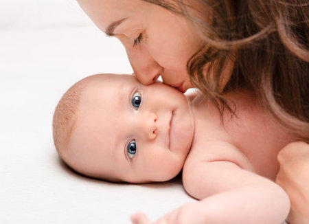 Mom sweetly kisses smiling baby on the cheek, close-upの写真素材