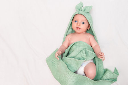 A cheerful baby lies in a towel with bunny ears after bathingの写真素材