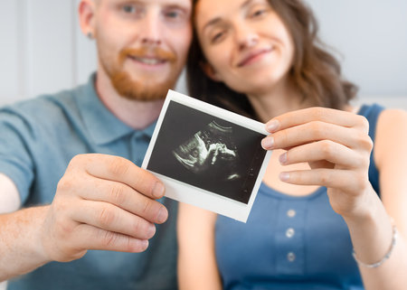 happy young parents show ultrasound photos of their future baby