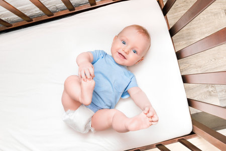 the baby lies on his back in a crib, holding his legsの写真素材