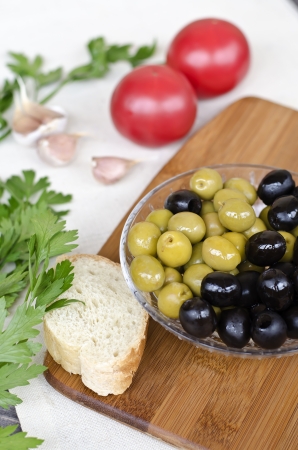 Fresh tomatoes, garlic, parsley and olives in a bowl on a wooden board.の写真素材