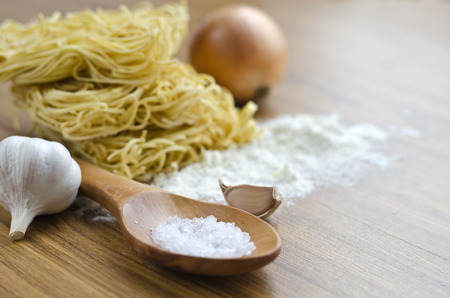 Three eggs and dry egg noodles on the kitchen table and a napkin with a wooden spoon. Ingredients for cooking noodles.の写真素材