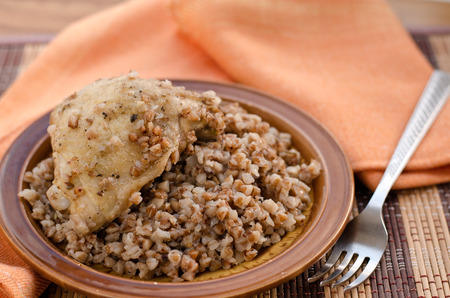 Stewed buckwheat with chicken on brown ceramic plate and orange napkin with a fork.の写真素材
