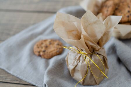 Oatmeal cookies with chocolate in parchment paper with a gold ribbon. On the table is a linen napkin.の写真素材