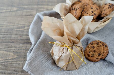 Oatmeal cookies with chocolate in parchment paper with a gold ribbon. On the table is a linen napkin.の写真素材