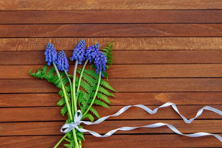 bouquet of blue Muscari with green fern leaves tied with white ribbon on wooden brown background top viewの写真素材