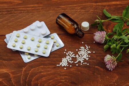 Pills scattered on the table from a glass bottle next to them are pills in a blister and a bunch of pink clover with flowers and green leaves a view from the top on a brown wooden backgroundの写真素材