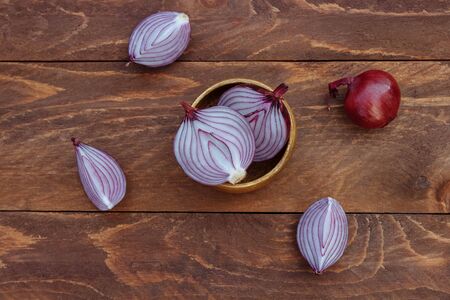 Red onions whole and cut in halves and quarters in a bowl on a brown wooden background top viewの写真素材