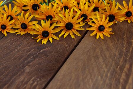 A bouquet of yellow daisies with a black center for congratulations lies on a brown wooden table with an empty space for textの写真素材