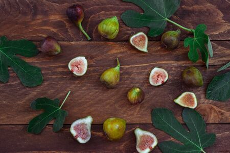 Ripe figs whole and cut in half with green leaves on a brown wooden background top viewの写真素材