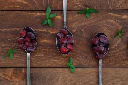 Red ripe frozen dogwood berries lie in tablespoons with green mint leaves on a brown wooden background view from the topの写真素材
