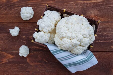 Cauliflower large heads lie in a rectangular wicker basket with a white napkin next to small inflorescences on a brown wooden background view from the topの写真素材