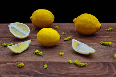 Yellow lemons whole and cut into slices and half on a brown wooden kitchen table with scattered wildflowers on a dark backgroundの写真素材