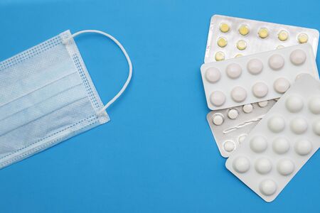 Disposable medical mask and tablets in blisters on a blue background top view with space for textの写真素材