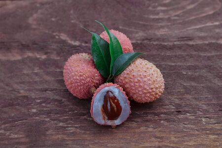 A group of ripe lychee berries whole and cut with a bone and white flesh, green leaves close-up on a brown wooden backgroundの写真素材