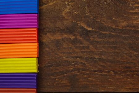 Multicolored smooth pieces of plasticine from the right on a brown wooden background with an empty space for the textの写真素材